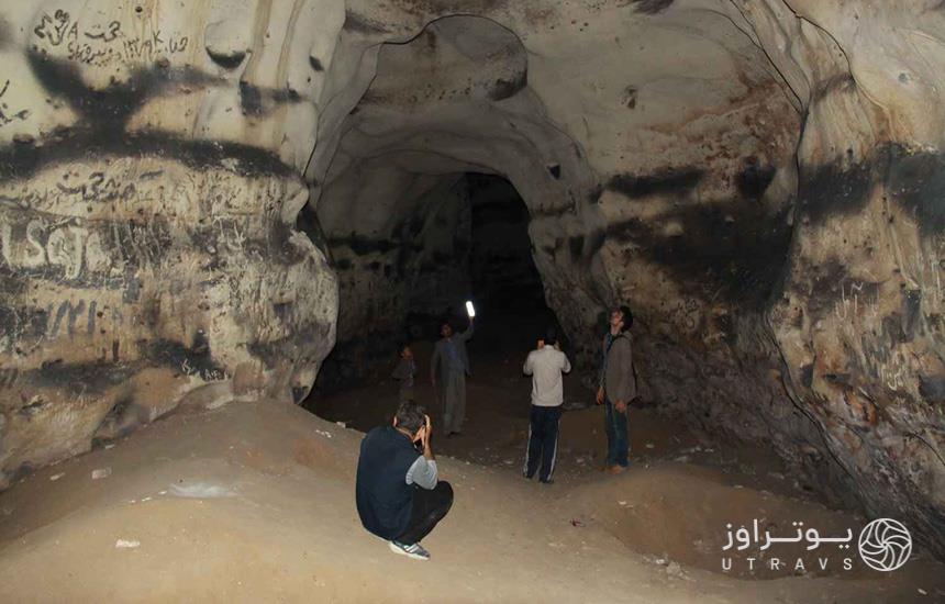 چهار مرد و یک پسربچه در غار بتخانه کوهدشت با زمینی ناهموار ایستاده و درحال تماشای دیواره‌های آن‌اند. 